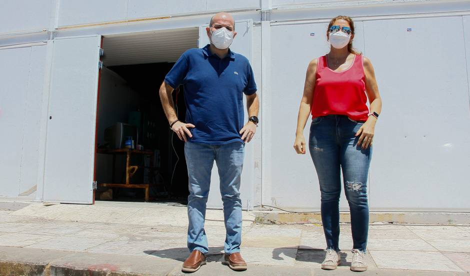 prefeito e secretária Dalila de máscara, em pé posando para a foto com obra de Escola Areninha ao fundo